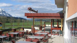 Une terrasse extérieure avec des tables et des chaises, un espace salon abrité et une vue sur les montagnes.