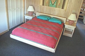 A single-bed room with a wooden headboard, two bedside tables with lamps, a red-striped bedspread, and a patterned wall hanging.