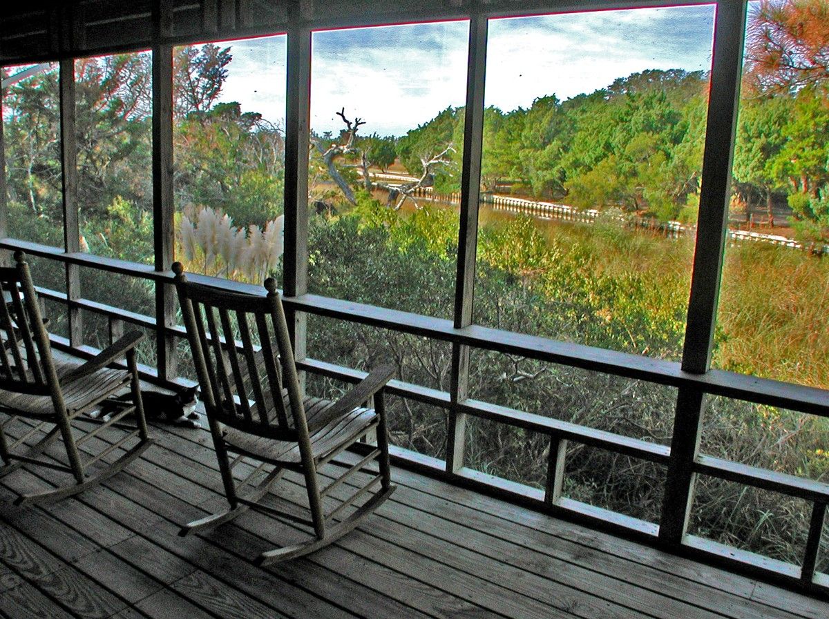 A wooden deck with rocking chairs overlooking a natural landscape.