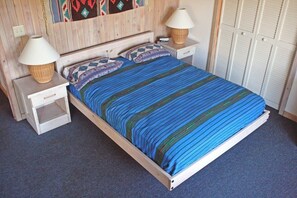 A single bed with a blue striped bedspread, two bedside tables with lamps, a wooden headboard, and a set of white lockers.