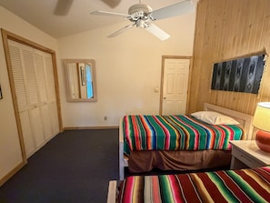 Un dormitorio con cama, ventilador de techo, una puerta y una obra de arte en la pared.