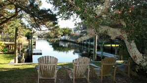 Un'area relax all'aperto con sedie e tavolo di legno, affacciata su un tranquillo specchio d'acqua, circondata da alberi e un pontile in legno.