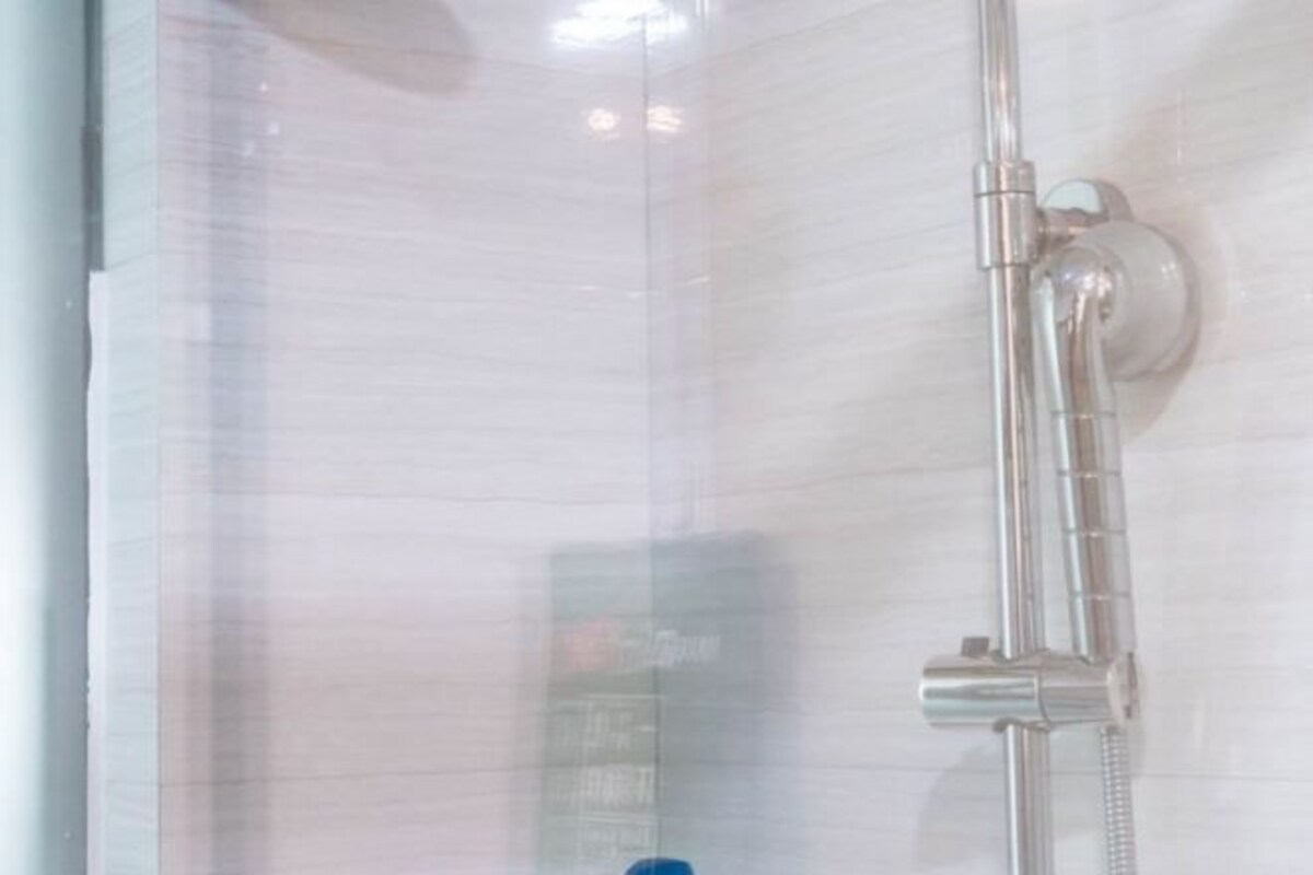 Une douche avec un flexible chromé et des commandes fixées au mur.
