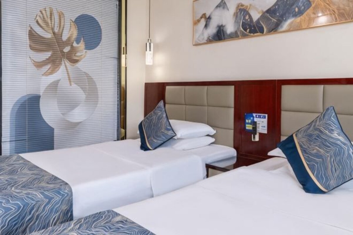 Une chambre d’hôtel avec deux lits, une tête de lit, un mur orné d’un motif de feuilles et un tableau.