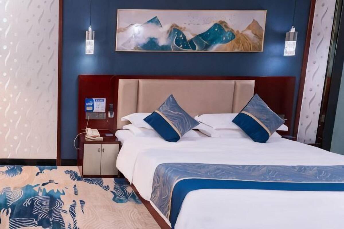Quarto de hotel com uma cama, mesa de cabeceira, telefone e um quadro na parede.