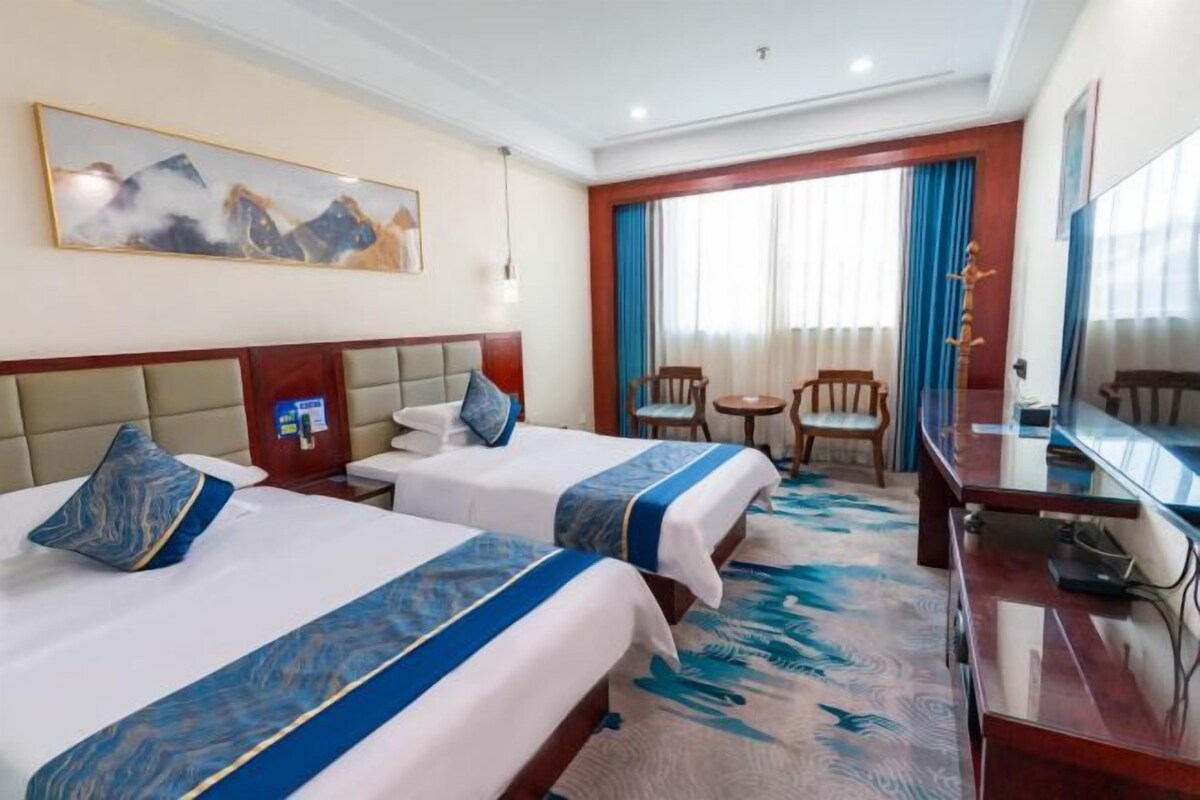 A hotel room with two beds, a desk, a chair, a small table, and a large window with curtains.