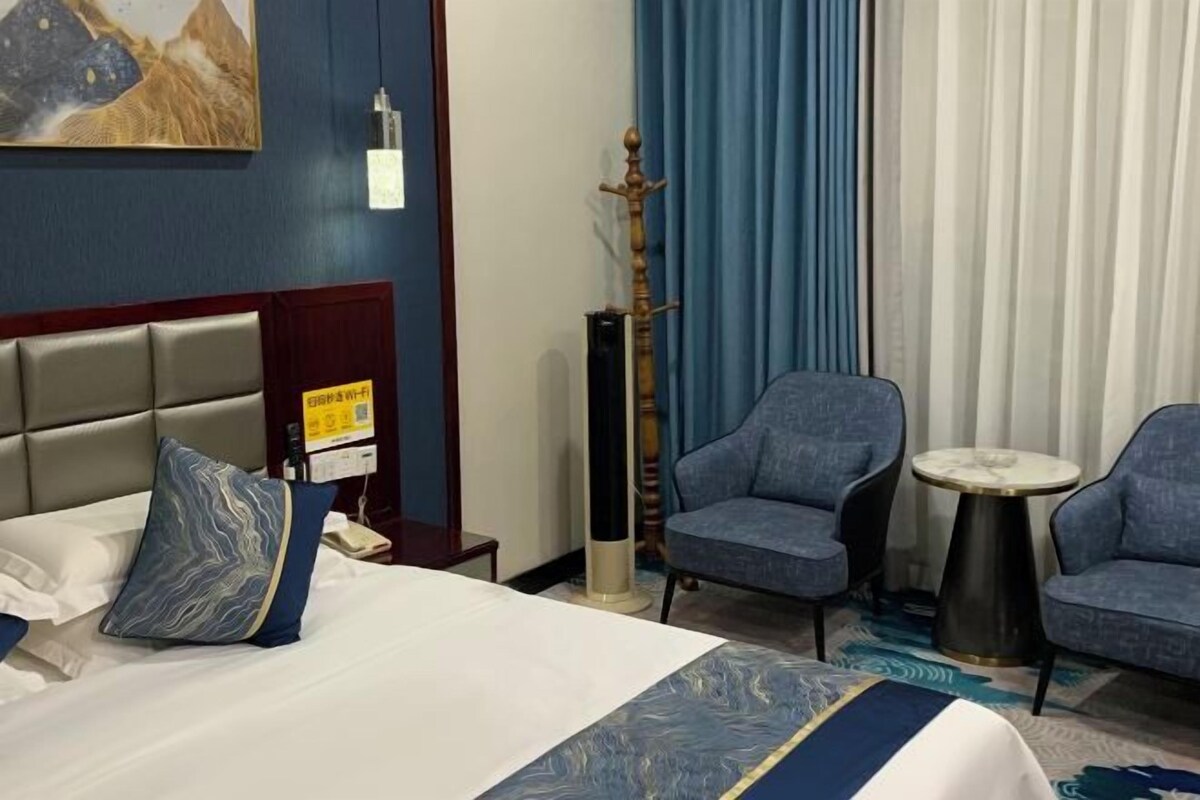 A hotel room with a bed, two armchairs, a small round table, a decorative pillar, and a painting on the wall.