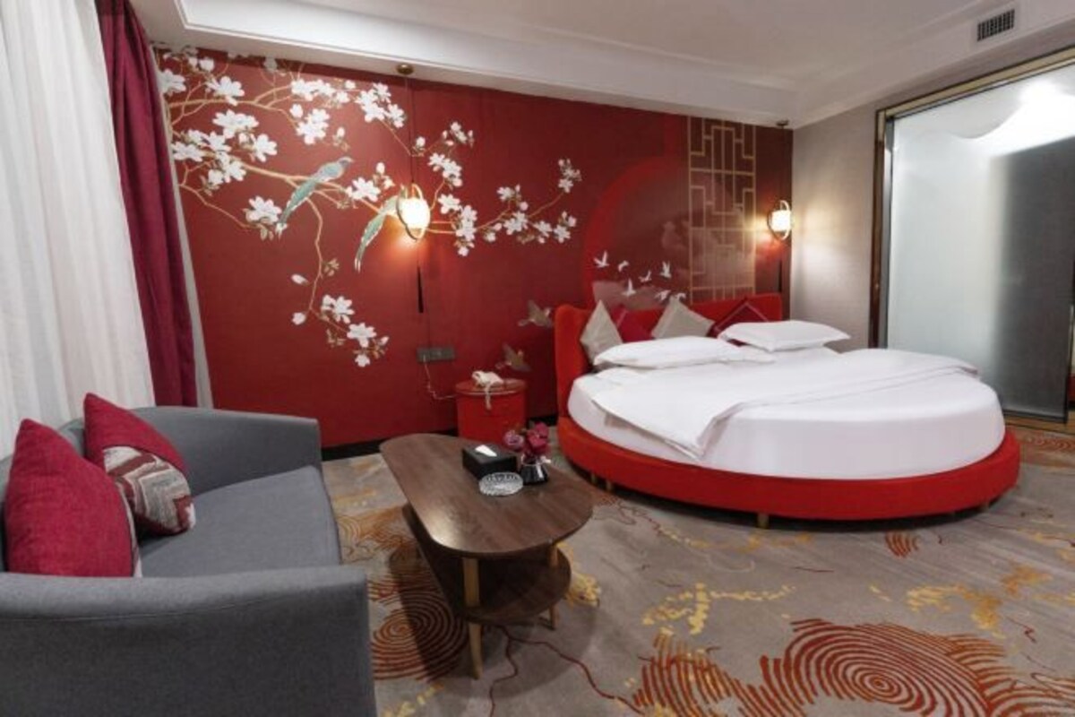 Une chambre d’hôtel avec un lit rond, un canapé, une petite table et un mur décoré d’œuvres d’art florales.