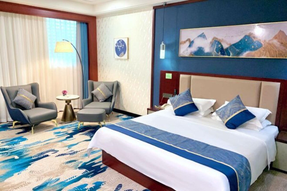 Une chambre d’hôtel avec un grand lit, deux fauteuils, une petite table ronde et un tableau au mur.