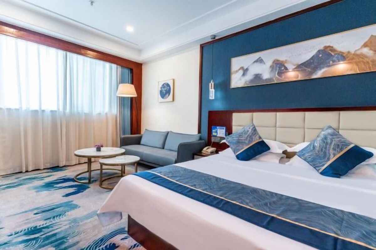 A hotel room with a large bed, a sofa, a small table, and a painting on the wall.