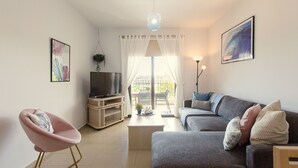 En moderne stue med sofa, lyserød lænestol, fjernsyn og spisebord.