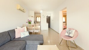 En moderne stue med en grå sofa, en rund pink farvet stol og et spiseområde med bord og stole.