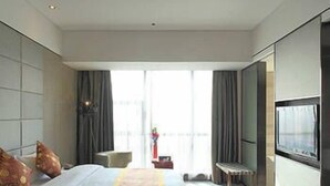 Habitación de hotel moderna con una cama grande, un televisor de pantalla plana y vistas a la ciudad a través de amplias ventanas.