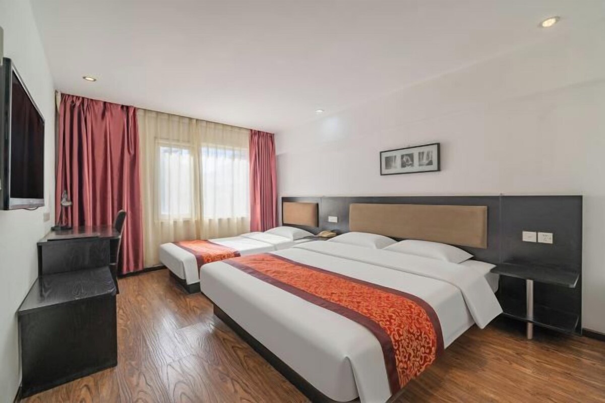 A hotel room with two beds, a desk, a chair, a TV, and a window with curtains.