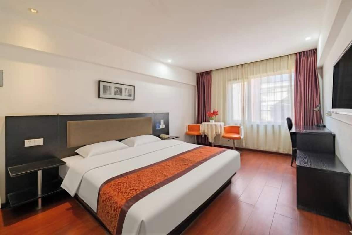 A hotel room with a bed, a desk, a chair, a TV, and a window with curtains.