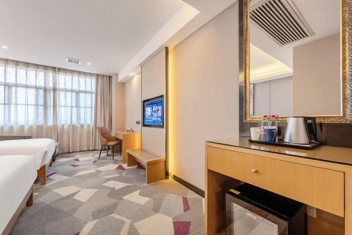 A hotel room with two beds, a desk, a chair, a TV, a coffee maker, and a mirror.
