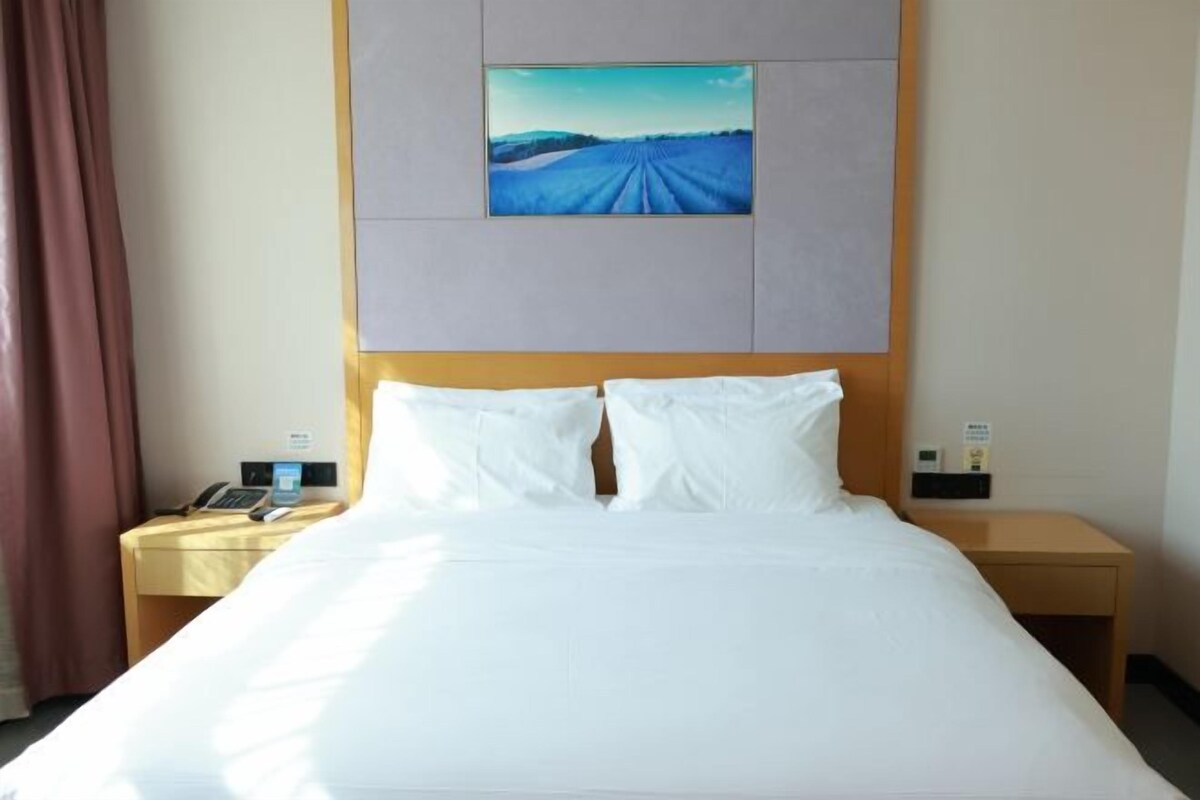 A hotel room with a large bed, a nightstand with a phone, and a painting on the wall.