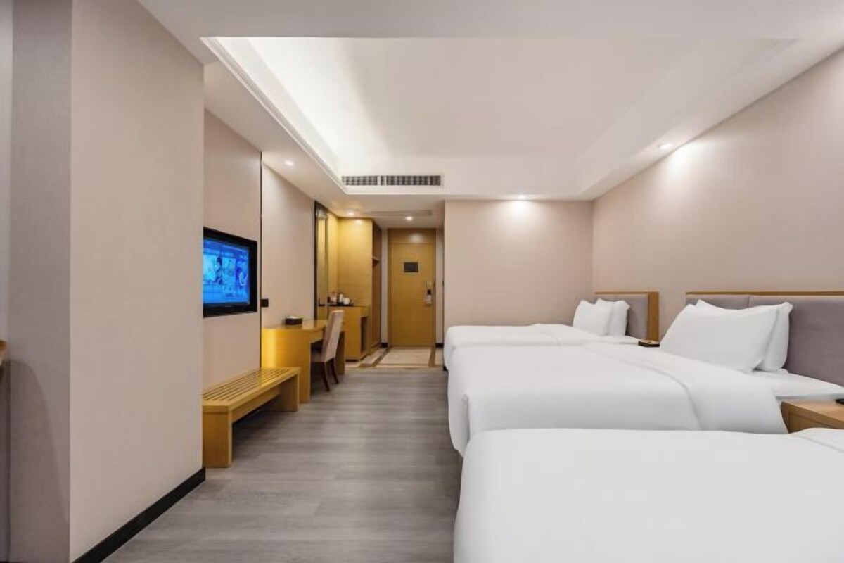 A hotel room with two beds, a TV, a desk, and a bench.