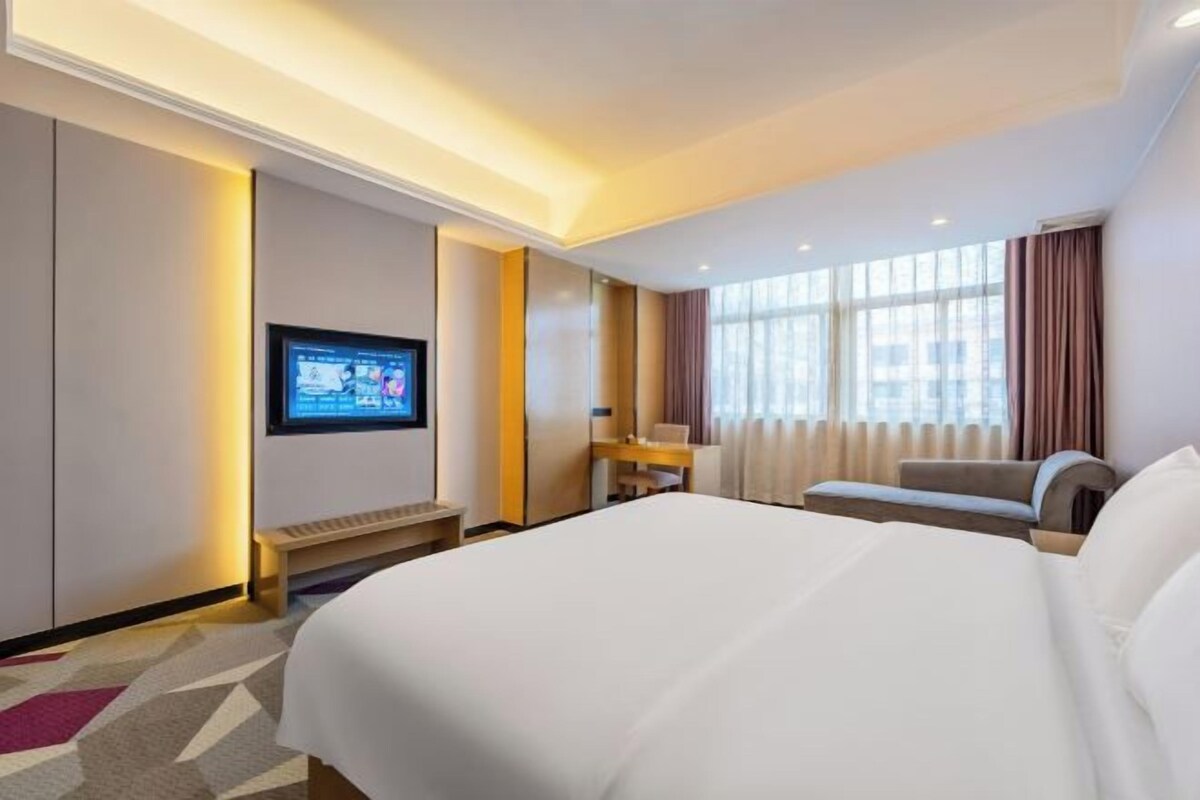 A hotel room with a large bed, a desk, a television, and a window with curtains.