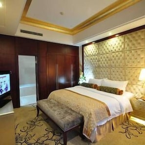 Une chambre d’hôtel avec un grand lit, un banc, une télévision et une armoire en bois.