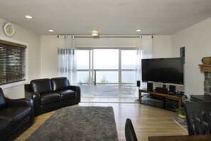Ein Wohnzimmer mit einem schwarzen Ledersofa, einem Flachbildfernseher und einem Kamin aus Stein.