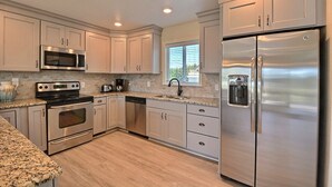 A modern kitchen with stainless steel appliances, white cabinetry, and a granite countertop.