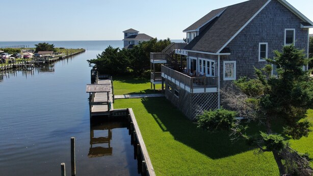 A waterfront property with a large house, a dock, and a grassy lawn.