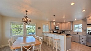 A modern kitchen with a central island, bar stools, and a dining table with chairs.