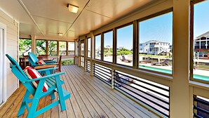 Un espace extérieur abrité doté d’un plancher en bois, de grandes fenêtres et de chaises Adirondack bleues.