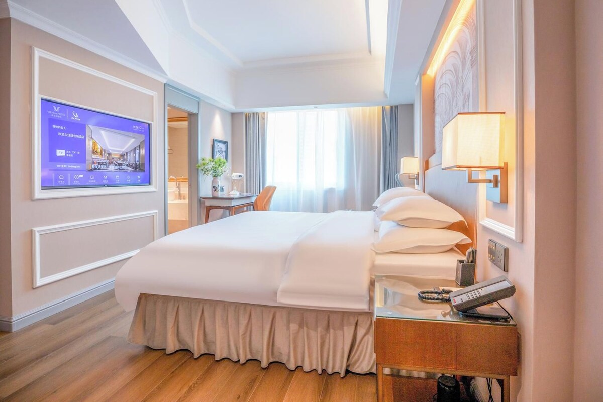 A hotel room with a bed, bedside table, TV, and a desk with a chair.