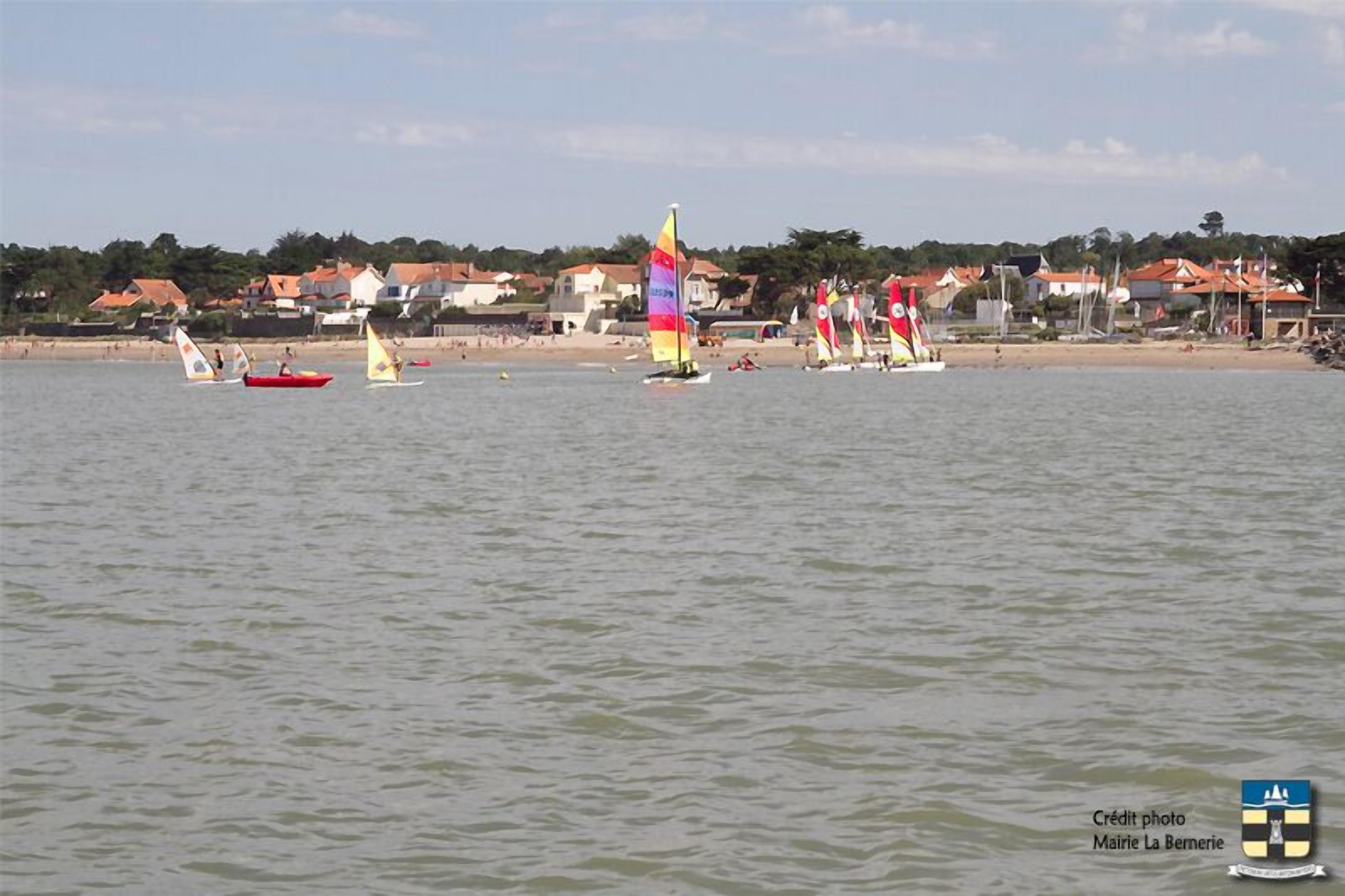 Een kustlandschap met zeilboten op het water, huizen op de achtergrond en een heldere lucht.