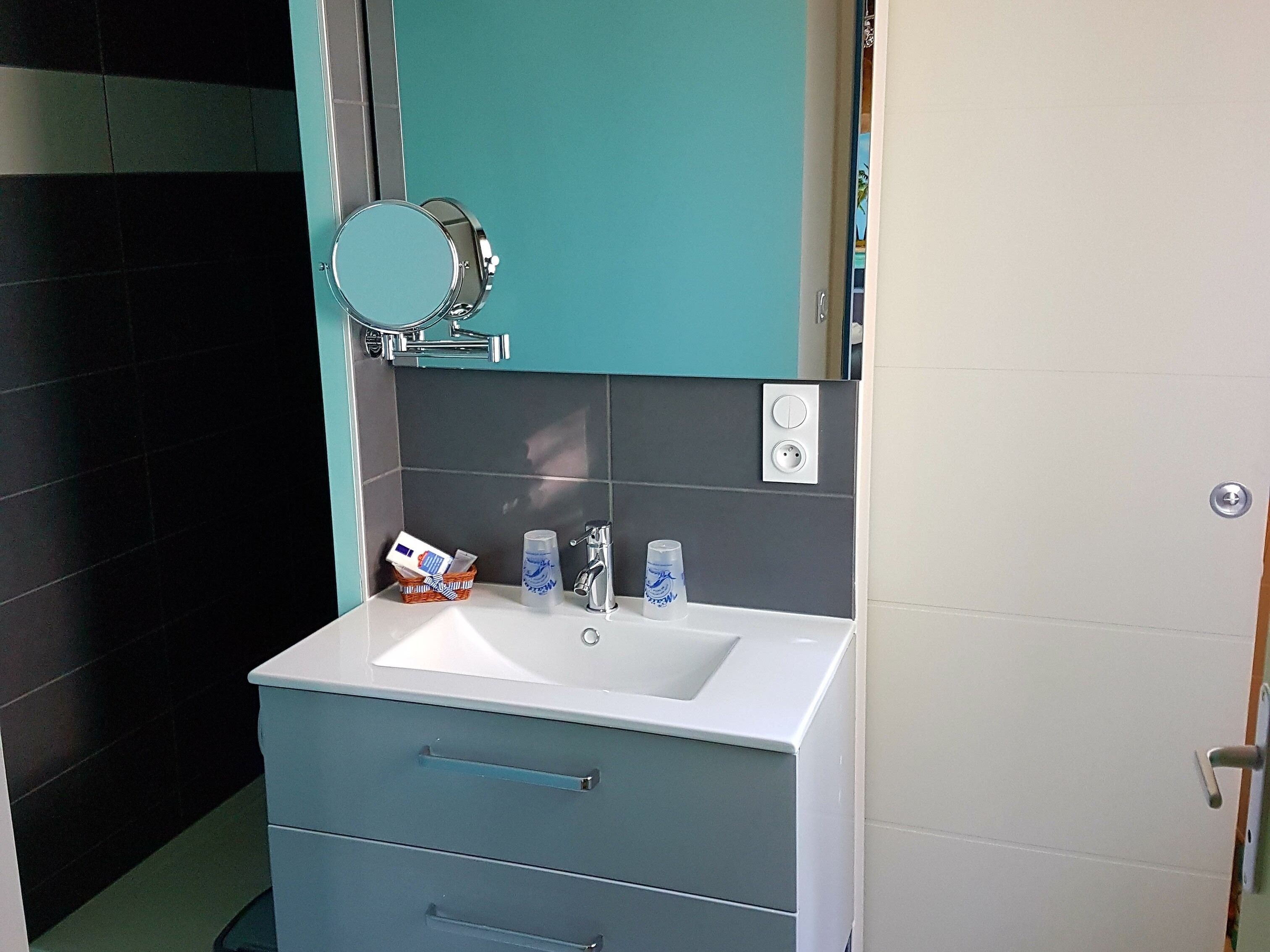 A bathroom with a white sink, a mirror, a teal cabinet, and a blue drawer unit.