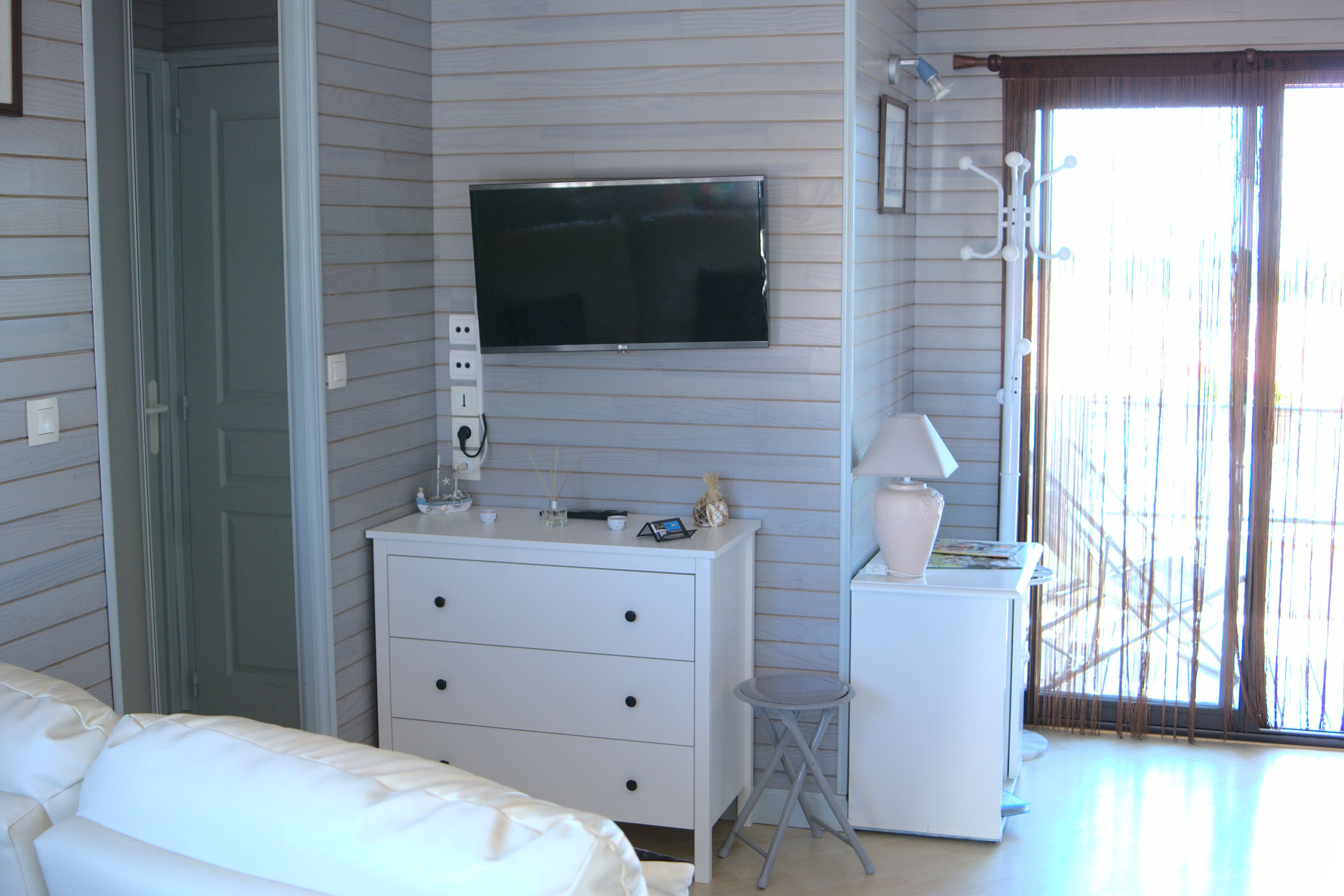 Een slaapkamer met een bed, een dressoir, een aan de muur bevestigde televisie en een raam met uitzicht.