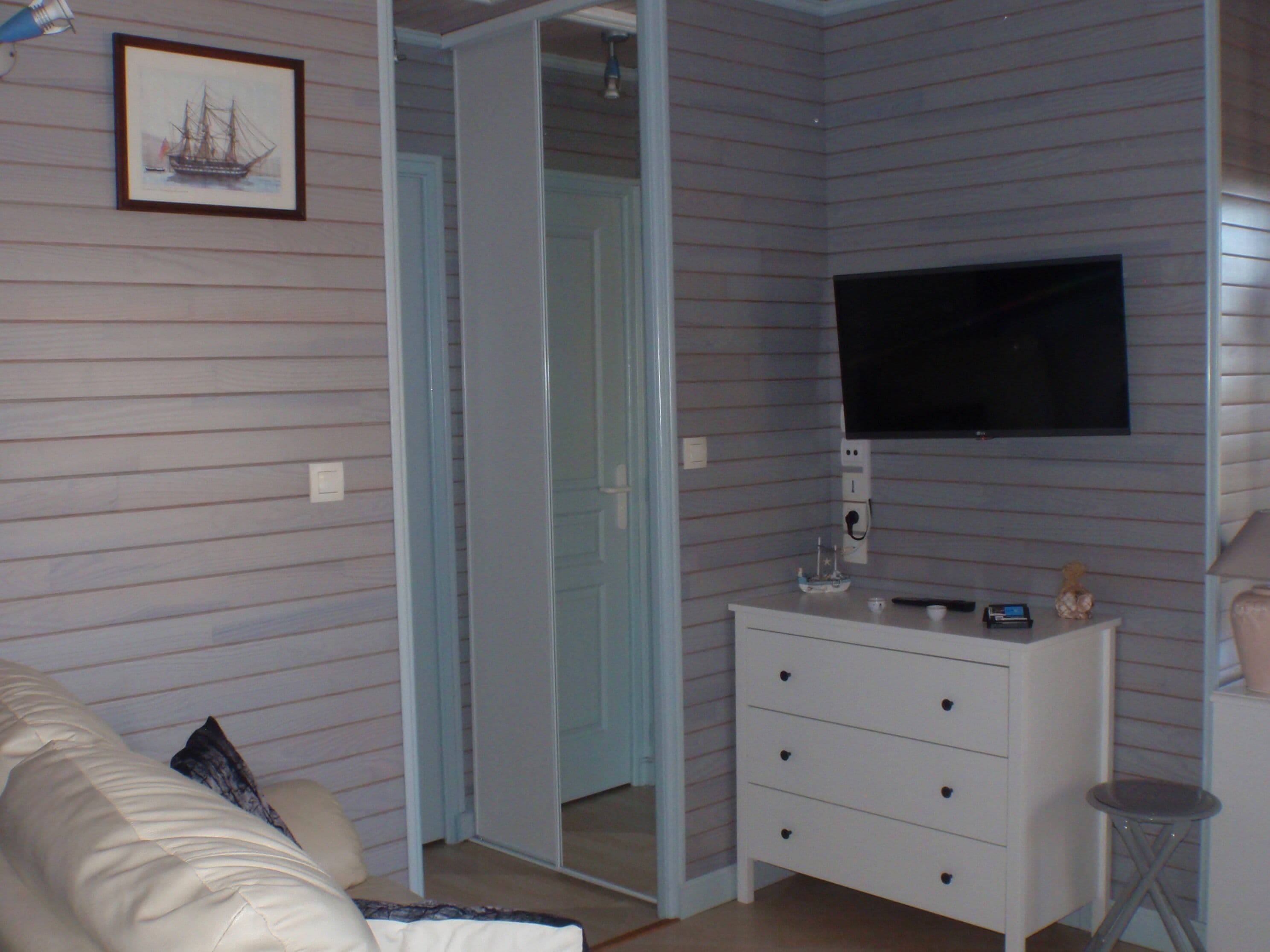 A room with a white dresser, a television mounted on the wall, and a framed picture of a ship.