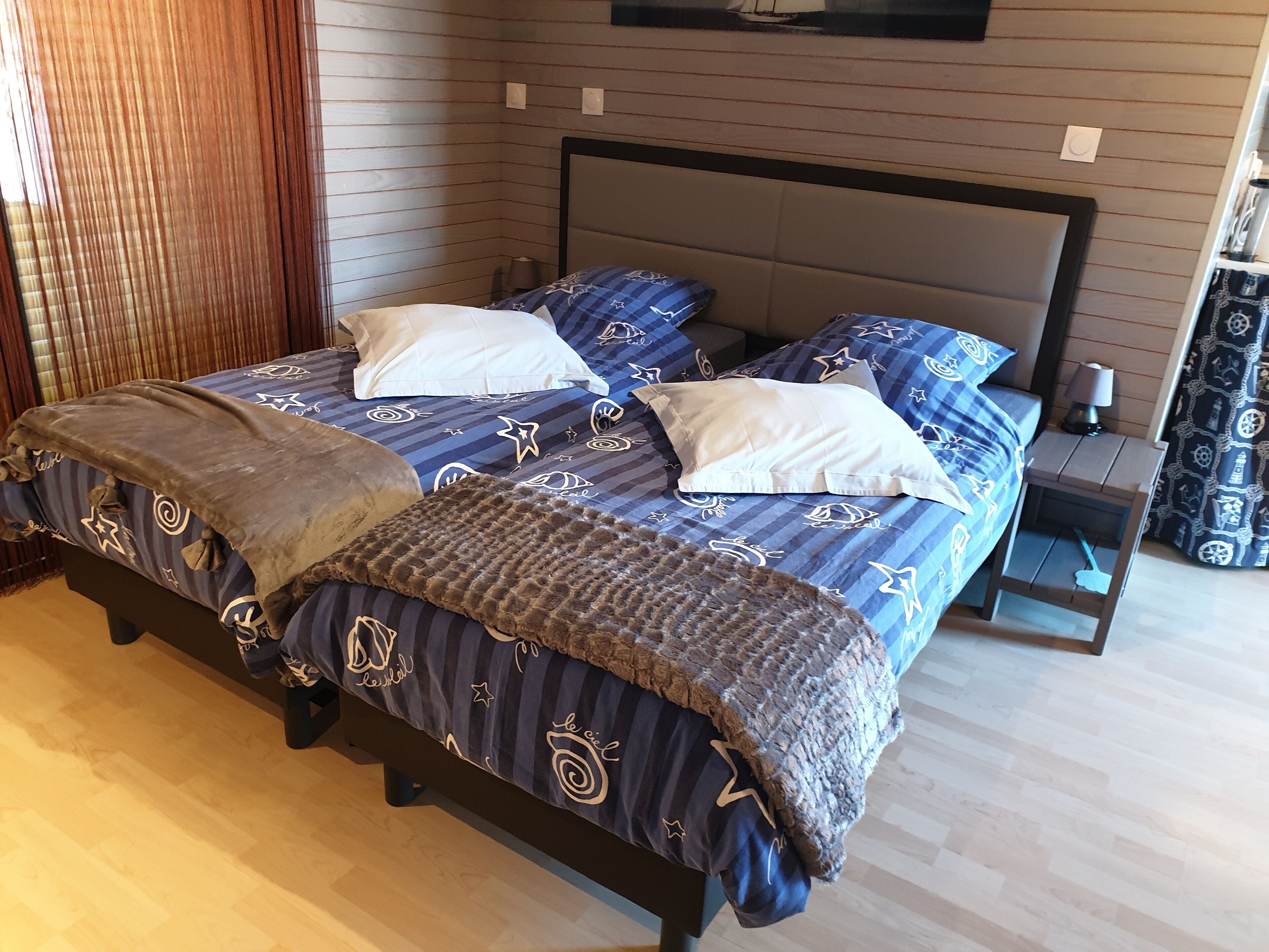 Un dormitorio con cama, almohadas, una manta, una mesita de noche y una lámpara.