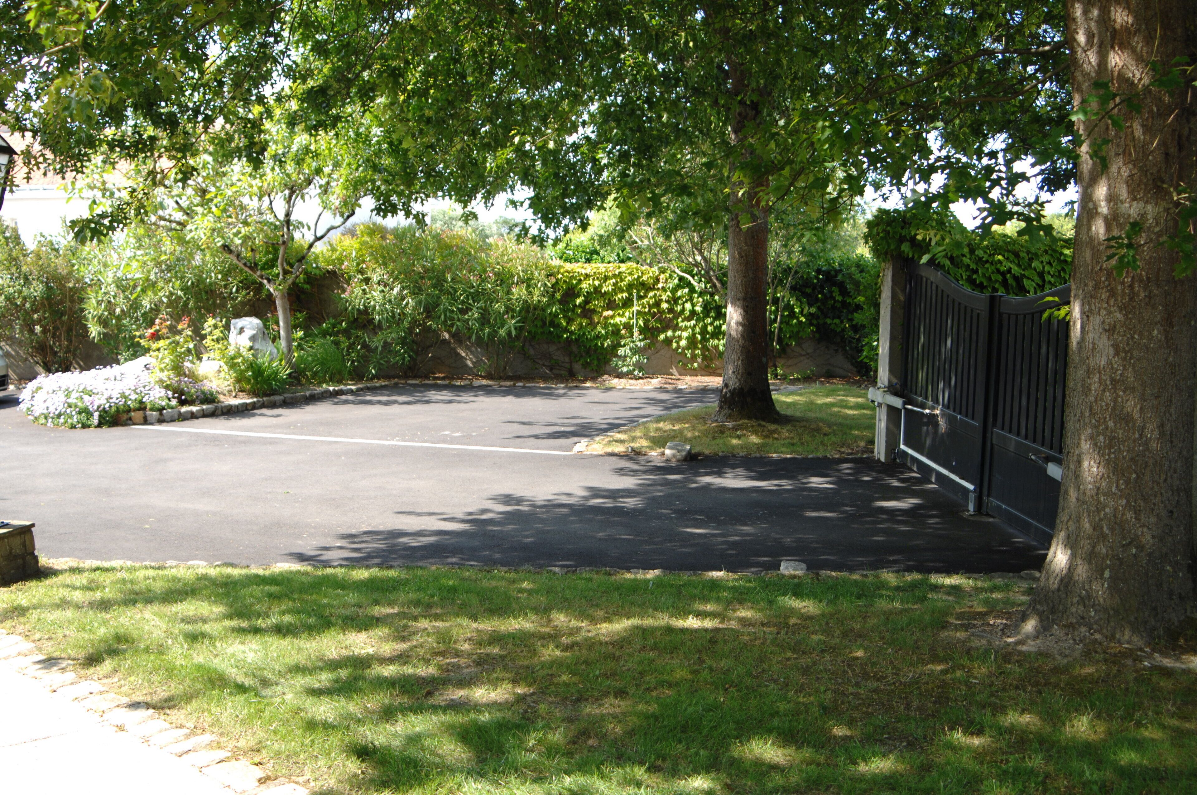 A paved driveway leading to a gated entrance, surrounded by lush greenery and trees.