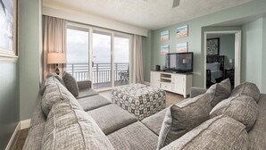 A spacious living room with a large sofa set, a television, and a balcony with a view. - Elite Beach Retreat - Ocean Walk (Daytona Beach)