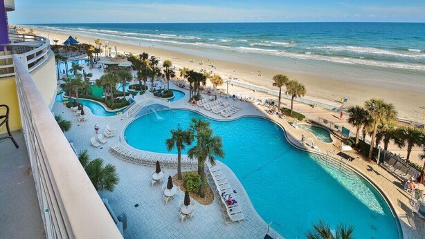 A resort with a large swimming pool, beach access, and palm trees. - Elite Beach Retreat - Ocean Walk (Daytona Beach)