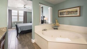A room with a large bathtub, a bed, a ceiling fan, and a window with curtains. - Elite Beach Retreat - Ocean Walk (Daytona Beach)