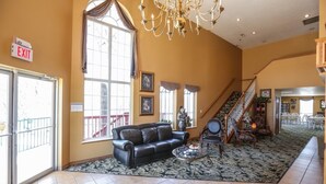 A spacious lobby with a black leather sofa, a coffee table, and a chandelier. There is a staircase leading to another level, and an exit sign is visible. - Presley's Penthouse 2BR Branson Resort Condo (Branson)