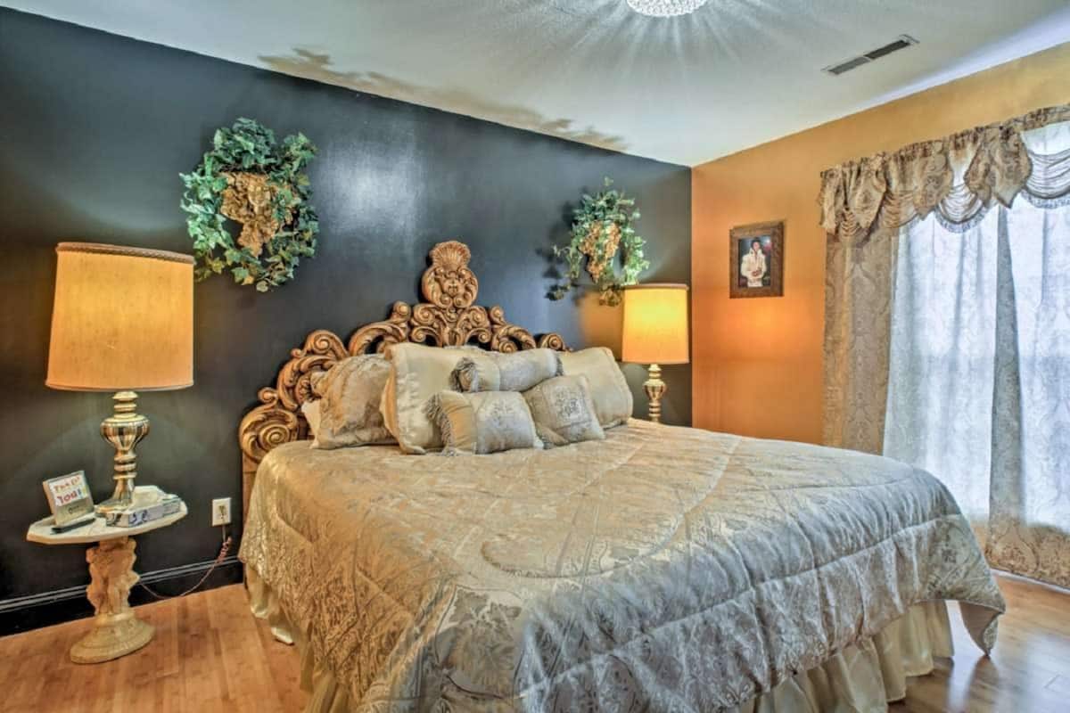 A bedroom with a large bed, two bedside lamps, a decorative headboard, and a framed picture on the wall.