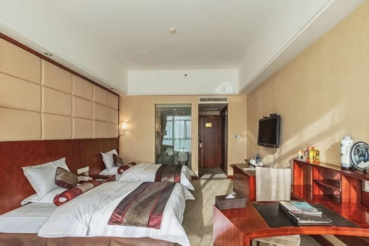 Ein Hotelzimmer mit zwei Betten, einem Schreibtisch, einem Fernseher und einer Tür zu einem anderen Raum.