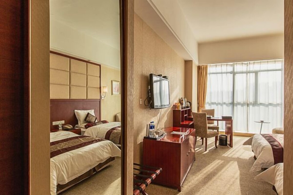 Ein Hotelzimmer mit zwei Betten, einem Schreibtisch, einem Stuhl, einem Fernseher und einem großen Fenster.