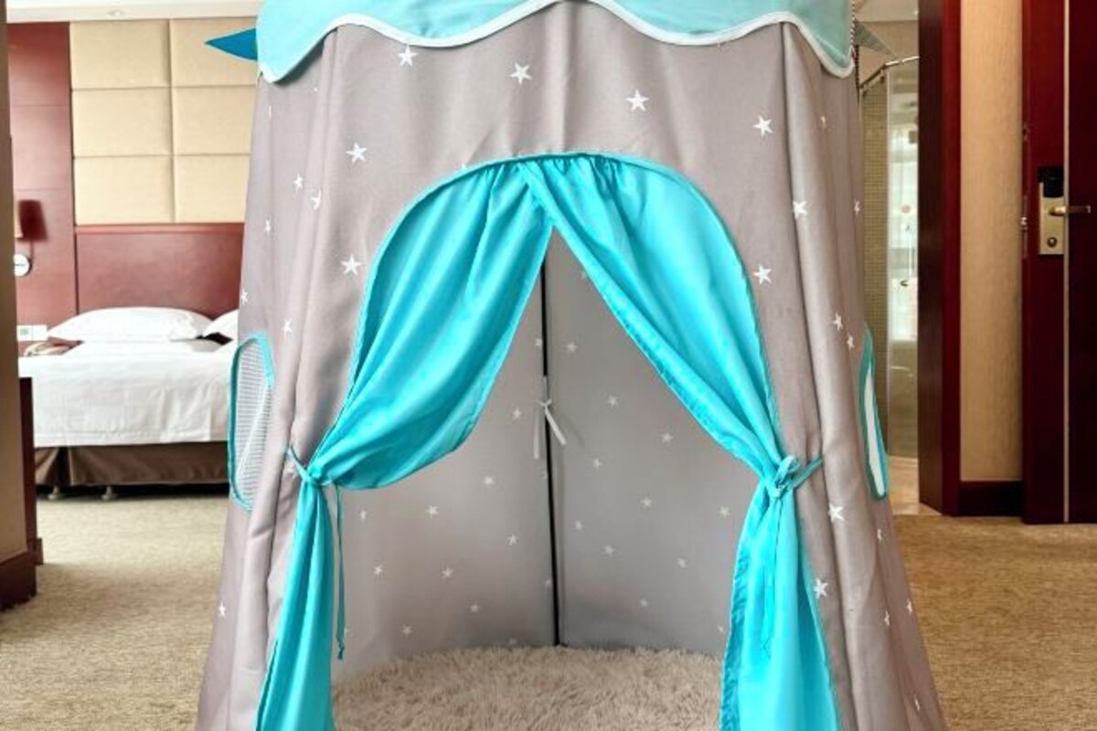 Een kamer met een bed, een zachte witte vloerkleden en een grijze hemelbed met turquoise gordijnen vastgebonden aan de voorkant.