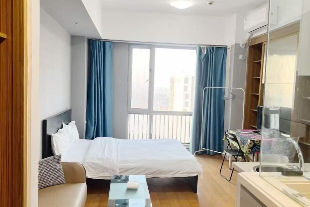 A hotel room with a bed, a small table, a desk, and a window with curtains.