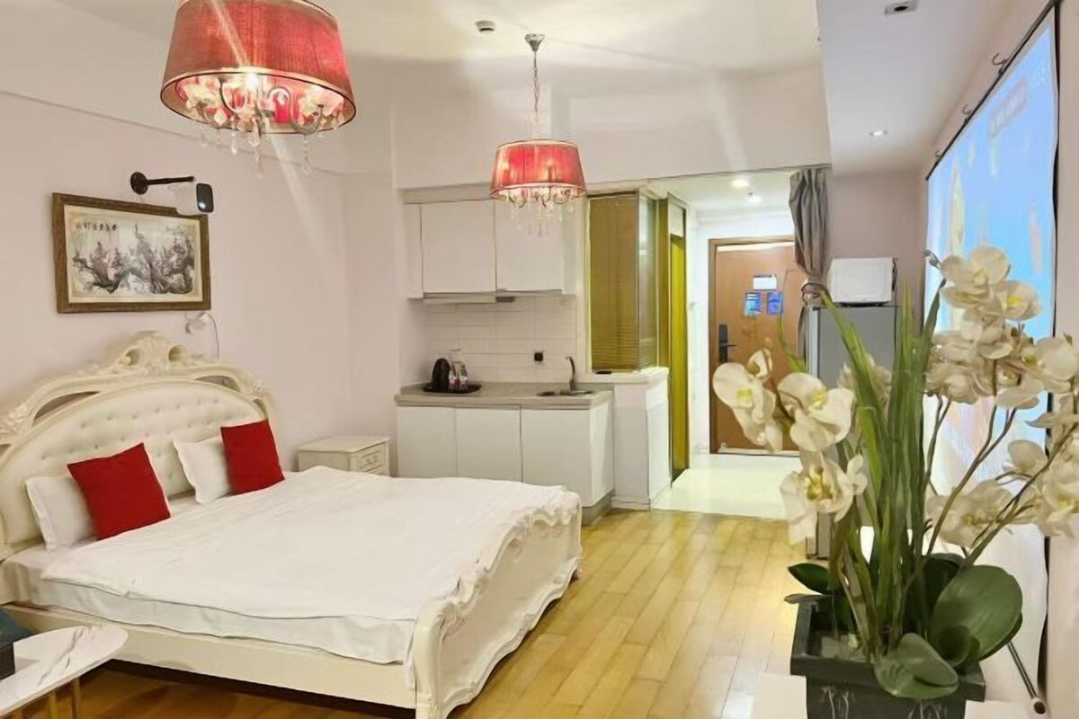 Un dormitorio con cama, mesita de noche, escritorio, candelabro, un cuadro en la pared y una planta en maceta.