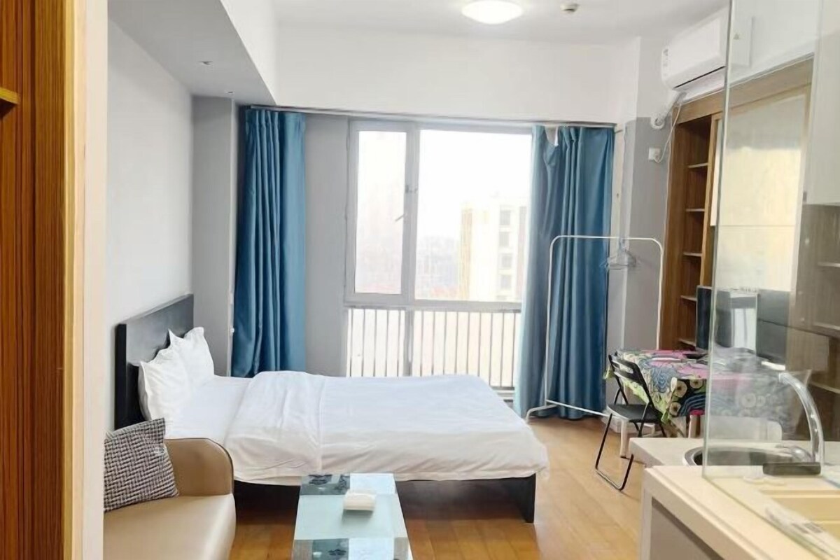 A hotel room with a bed, a small table, a desk, and a window with curtains.