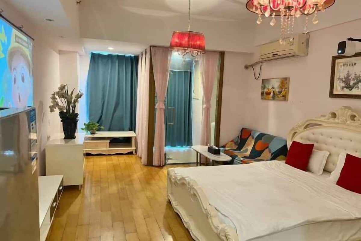 A hotel room with a bed, a television, a desk, a chair, a sofa, and a chandelier.