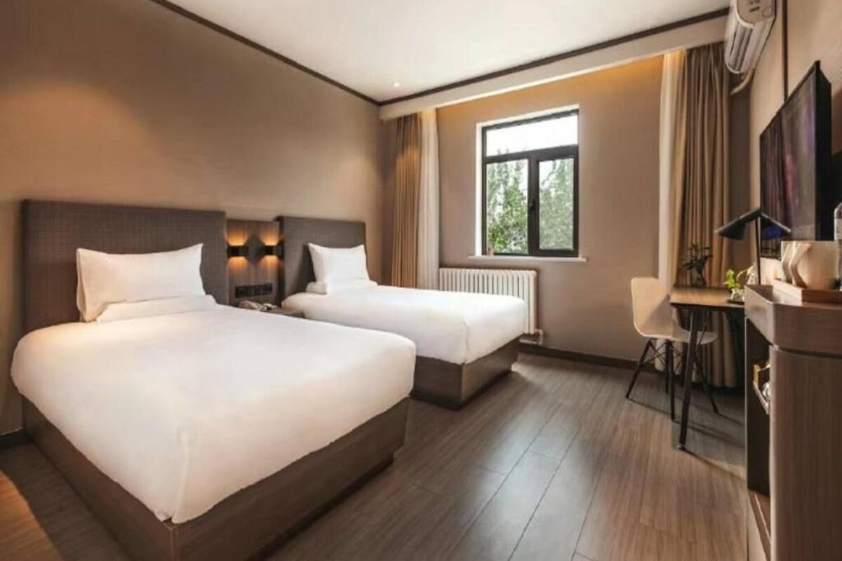 A hotel room with two beds, a desk, a chair, a window, and a radiator.