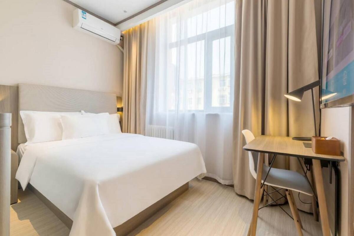 A hotel room with a bed, a desk, a chair, a TV, and a window with curtains.